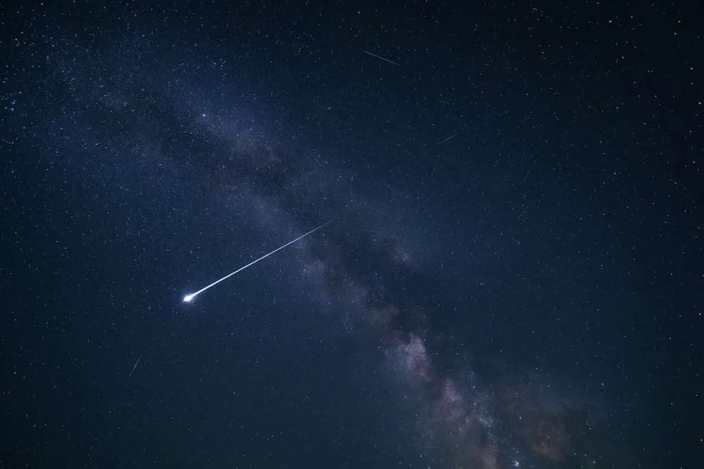 Ilustrasi hujan meteor Orionid melintas di langit malam yang gelap dengan gugusan bintang Orion sebagai latar