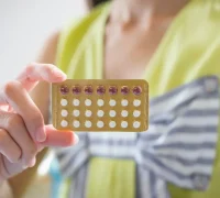 Ilustrasi perempuan memegang pil KB sebagai kontrasepsi hormonal dan simbol kesadaran terhadap kesehatan payudara. (freepik.com/jcomp)